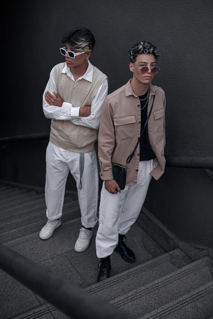 Stylish young men in beige and white outfits posing on stairs, embodying modern fashion trends.