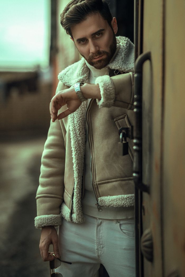 Fashionable man in shearling jacket checking time in a cityscape. Modern and stylish portrayal.