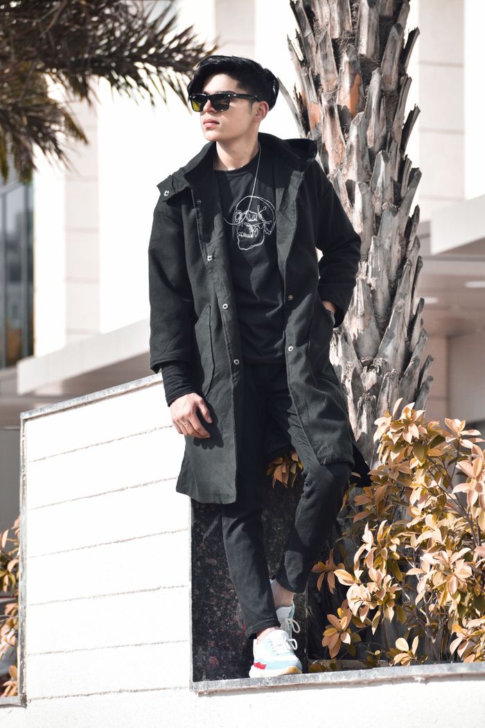 A fashionable man in black attire standing confidently outdoors, showing off his unique style.