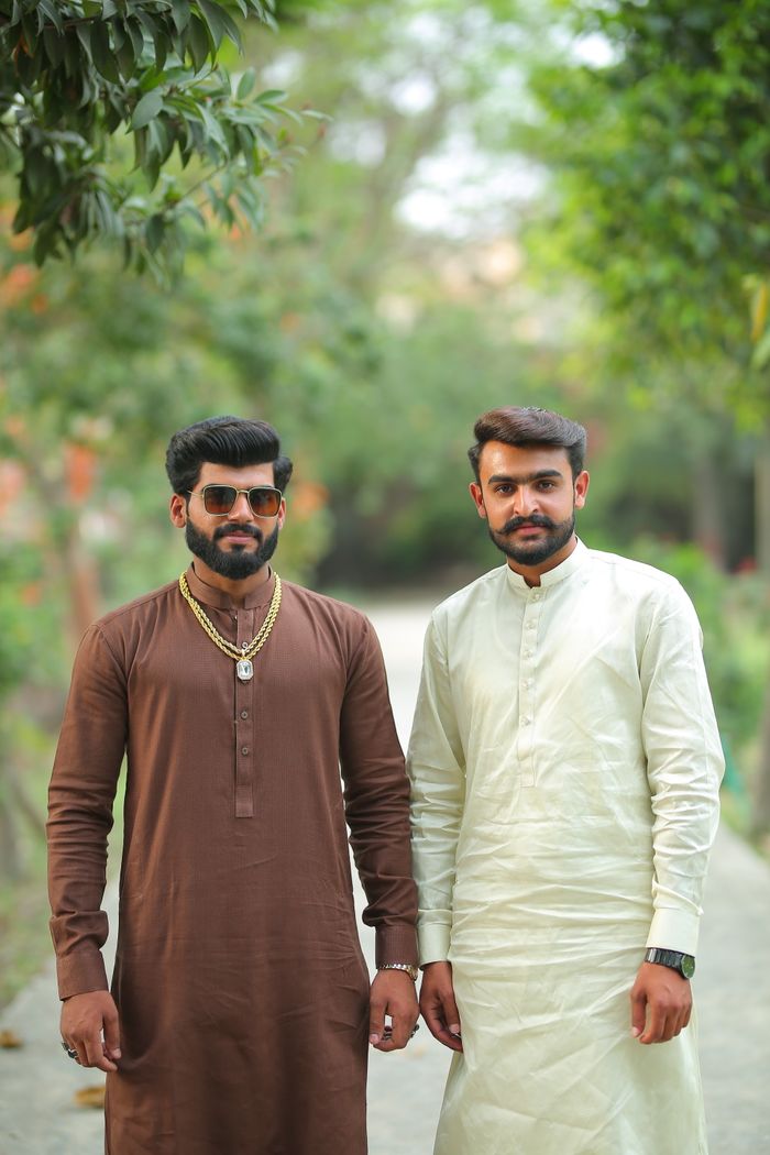Two men wearing traditional Pakistani robes standing outdoors, showcasing cultural fashion.